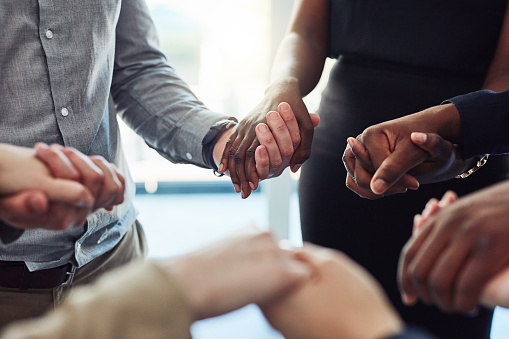 Cropped shot of a group of businesspeople standing together and holding hands in a modern office